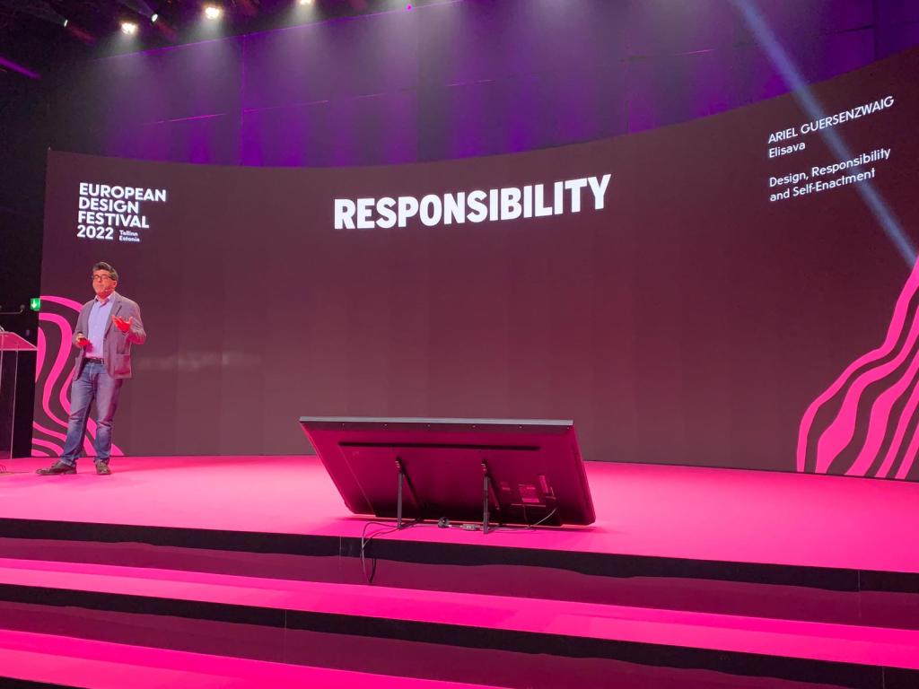 The image shows a speaker on a brightly lit stage at the European Design Festival 2022 in Tallinn, Estonia. The stage has a vibrant pink design, and the backdrop prominently displays the word "RESPONSIBILITY" in bold white letters, along with the speaker's name, Ariel Guersenzvaig, and the title of the talk: "Design, Responsibility, and Self-Enactment" The speaker is casually dressed, addressing the audience in a professional setting focused on design and ethics.